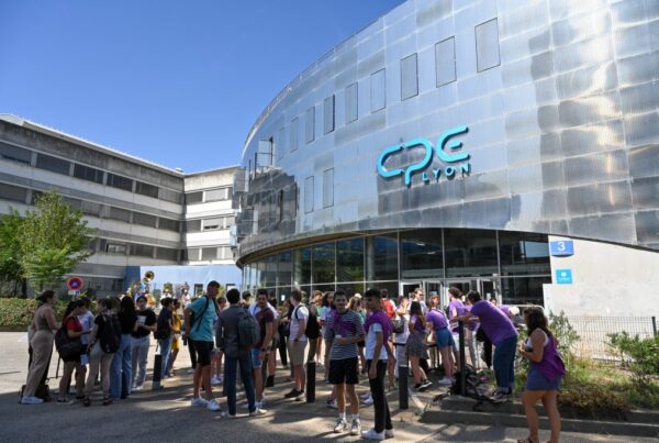 Groupe d'étudiants rassemblés devant l'entrée moderne du bâtiment CPE Lyon par une journée ensoleillée.